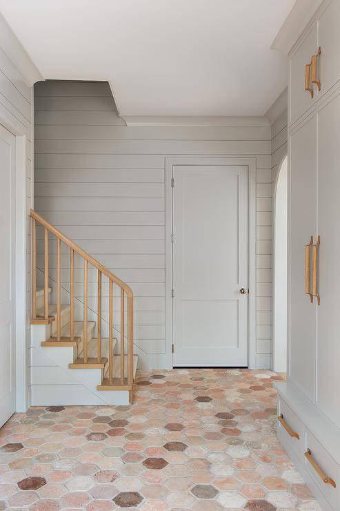 Terracotta hexagon pavers accent a mudroom boasting light light gray built-in cabinets accented with wood and leather pulls.