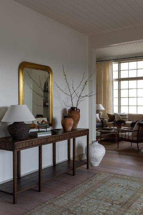 A gold leaf beaded mirror is mounted over a walnut console table with terracotta vases and a vintage runner.