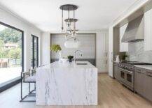 An eye-catching staggered chandelier is mounted over a white and gray marble waterfall edge kitchen island seating black and white stools.