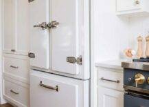 Kitchen features a white vintage refridgerator with satin nickel vintage latches surrounded by white cabinetry.