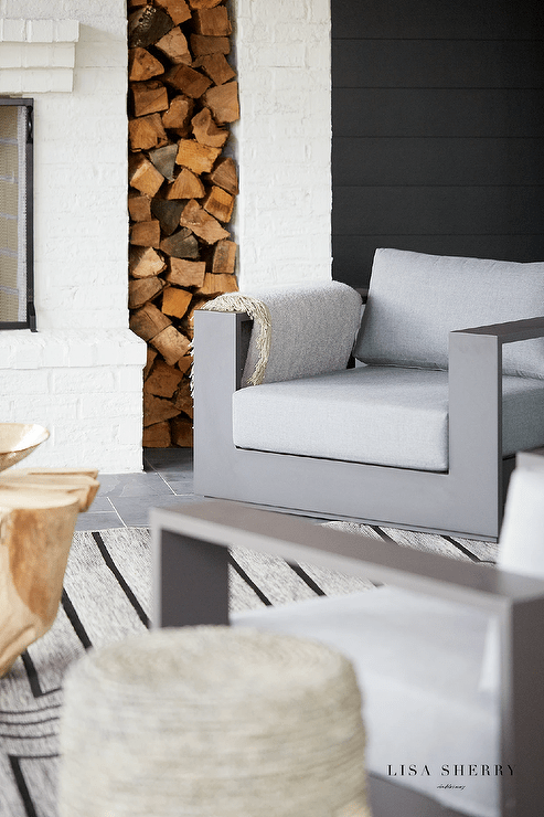 Living room features gray aluminum lounge chairs on a gray and black striped rug and a fireplace with built in wood storage.