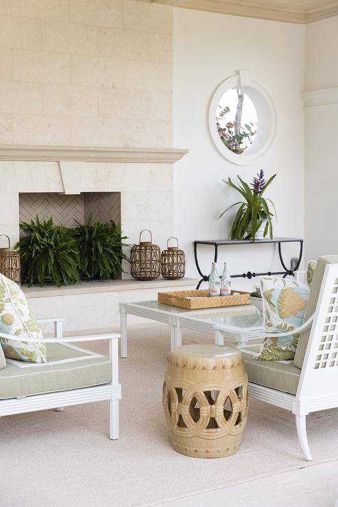 White aluminum lounge chairs with green and white cushions are placed on a beige outdoor rug and matched with beige rope stools in a gorgeous covered patio.