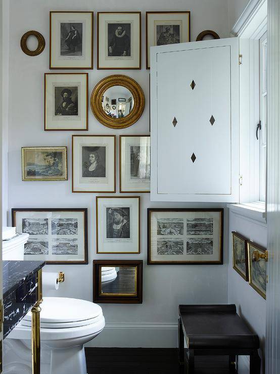 Stunning eclectic French country powder room boasts a marble and brass sink vanity positioned beside a white porcelain toilet located next to an art gallery wall.
