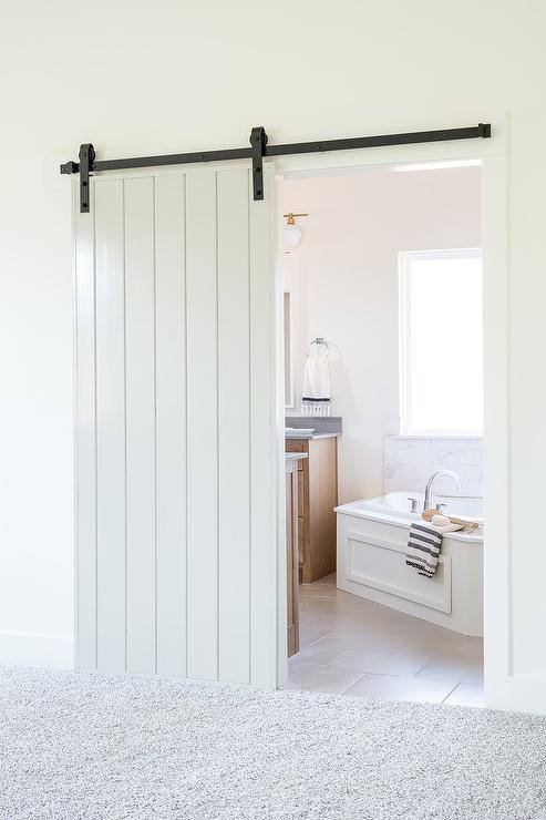 A white plank barn door on rails opens to a bathroom.