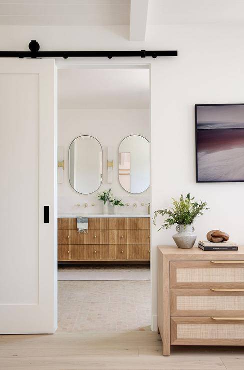 A white barn door on black rails is finished with oil rubbed bronze hardware opens to a reveal a beautifully appointed master bathroom.