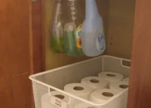 tension rod under bathroom sink with toilet paper and spray bottles