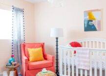 Orange and blue nursery boasts a bright blue vintage rug with a woven round pouf and a hot pink accent chair beside a white wooden crib. A white capiz chandelier adds a contemporary finish to the sweet nursery space.