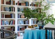 Staircase landing library features an azure blue fringe skirted table with potted plant and built in bookshelves.