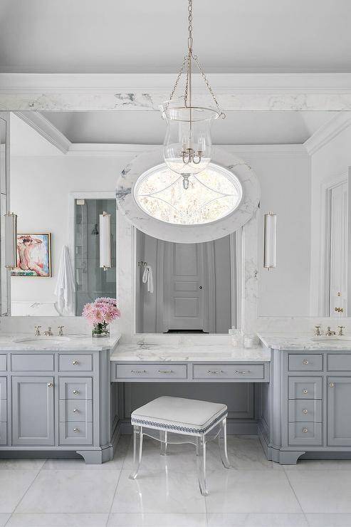 A French lucite stool stands in front of a gray makeup vanity topped with white and gray marble.