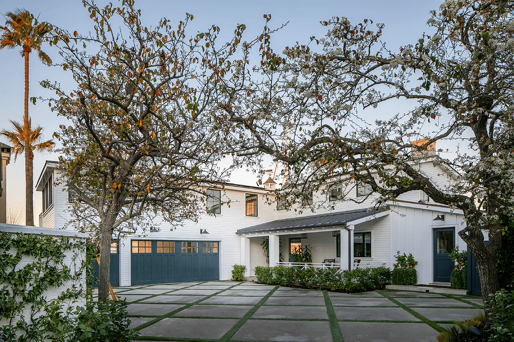 Concrete pavers framed by glass lead to an attached garage boasting blue doors accenting a white home.