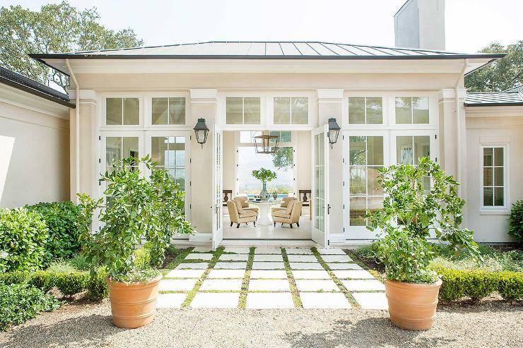 Lemon trees and terracotta planters sit in front of concrete pavers leading to a glass paneled double front doors lit by lantern sconces.