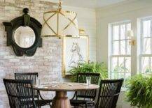 Cottage sunroom design features black wicker chairs at a brown oak pedestal game table atop red brick pavers illuminated by a Grosvenor single brass and white pendant.