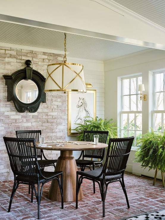 Cottage sunroom design features black wicker chairs at a brown oak pedestal game table atop red brick pavers illuminated by a Grosvenor single brass and white pendant.