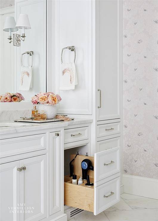 Hairdryer cabinet adds a unique pull out drawer feature to a white vanity washstand. The master bath vanity is completed with polished nickel hardware and marble countertops styled with decor for a sophisticated finish.