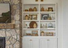 An antique brass picture light illuminates styled built-in shelves fixed above white plank cabinets.