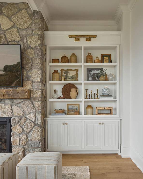 An antique brass picture light illuminates styled built-in shelves fixed above white plank cabinets.