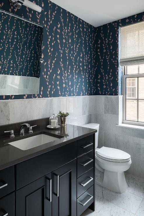 Gray marble offset wall tiles cover half of bathroom walls finished with Harlequin Salice Wallpaper, as a pivot mirror is mounted above a black washstand donning polished nickel pulls and a polished nickel faucet fixed to a black quartz countertop.