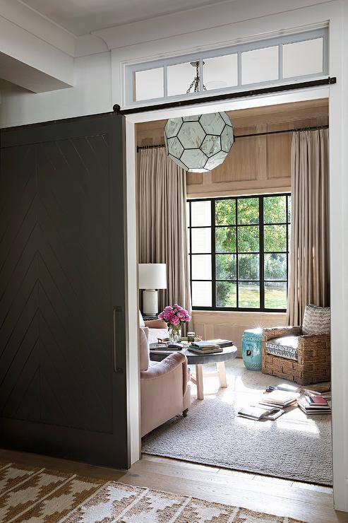 A black chevron door on rails positioned under transom windows opens to a welcoming family room.