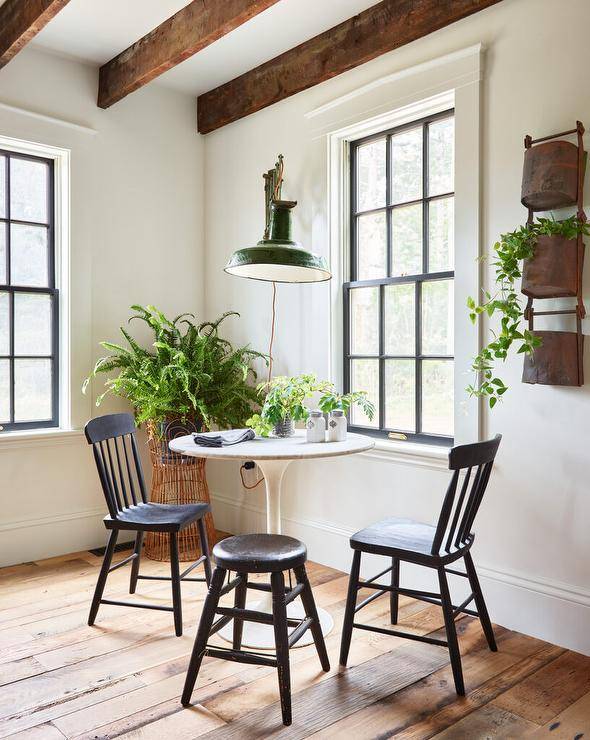 Dining space features a green accordion style lantern that illuminates a marble tulip table with vintage black spindle chairs under wooden ceiling beams.