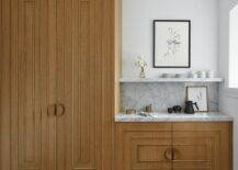 Chic pantry features gold, art deco style cabinets adorned with half moon, brass hardware. A marble backsplash and shelf sits over a coffee station.