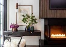 Black desk with black wishbone chair sits next to vintage style fireplace.