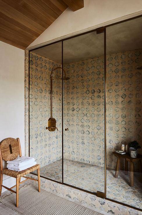 A walk in shower with a glass and brass enclosure boasts an eye-catching vintage brass shower kit mounted to Moroccan style surround tiles over matching floor tiles.