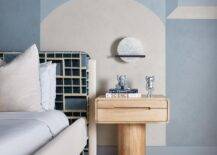 A charming white and blue wall is fixed behind a pedestal nightstand placed beside a vintage style bed positioned on a white and blue rug.