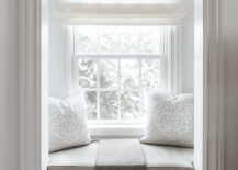 Small window seat nook is accented with a taupe cushion and pillows and a taupe linen throw blanket.