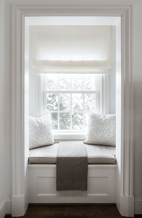 Small window seat nook is accented with a taupe cushion and pillows and a taupe linen throw blanket.