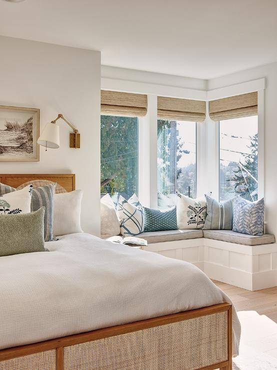 Bedroom features an L shaped window seat bench accented with blue pillows and a vintage wood and cane bed.