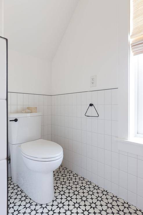 Half tiled vertical walls with black trim in a black and white bathroom boasting cement floor tiles under a vaulted ceiling.