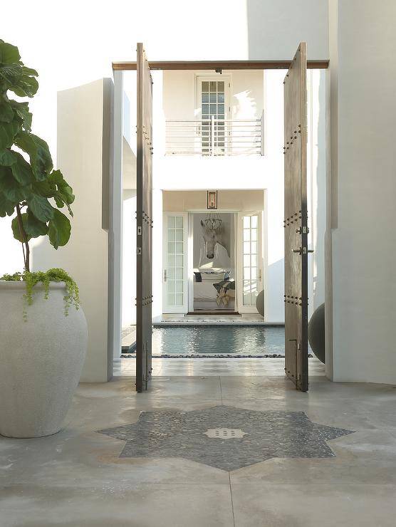 Moroccan style floor tiles lead through industrial pivot doors to an in ground swimming pool.