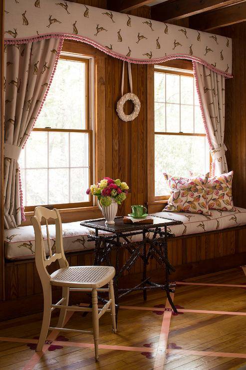 Vintage style bedroom features a black bamboo accent table with white French cane seat chair next to a built in window seat with rabbit print cushion under a rabbit print valance with matching curtains.