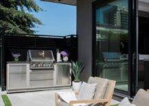 Stylish patio features stainless steel mini bbq kitchen, blond teak outdoor chairs with taupe cushions atop concrete pavers.