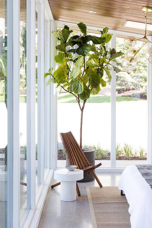 Sunroom as a bedroom features an oak plank ceiling, a wooden accent chair and a small white pedestal accent table.