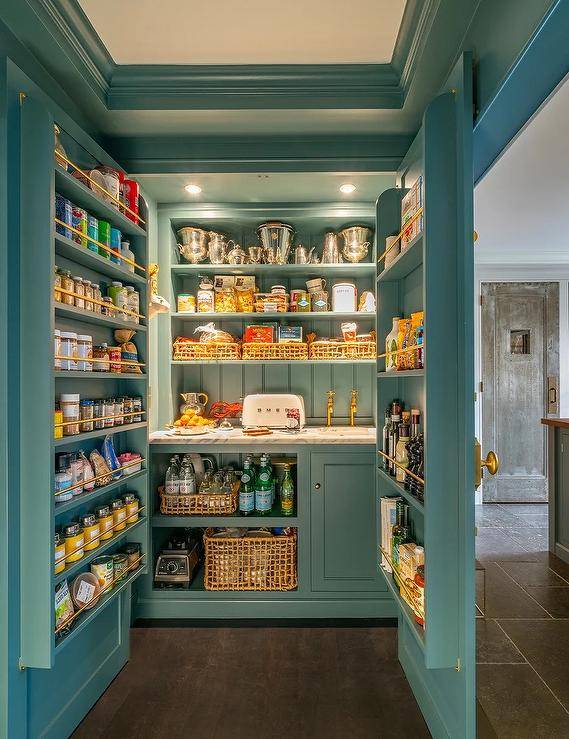 Dual blue small walk in pantry doors lined with spice shelves open to a well-organized and stocked pantry. Small kitchen pantry features a small sink paired with a brass, French style faucet as well as vertical blue shiplap trim.