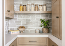 Brown floating shelves are stacked against a stone backsplash and between and over brown cabinets adorned with brass knobs.