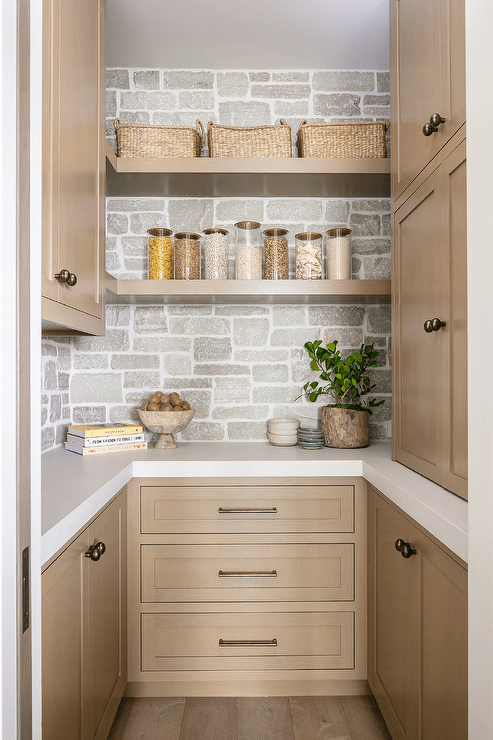 Brown floating shelves are stacked against a stone backsplash and between and over brown cabinets adorned with brass knobs.