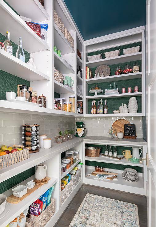 Green wallpaper accents the back of white pantry shelves fixed on either side of gray staggered backsplash tiles and beneath a peacock blue painted ceiling. Lower shelves are finished with a marble countertop.