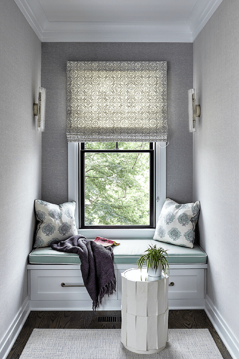 Window seat nook design with gray wallpaper features green seat cushions and blue block print pilows.