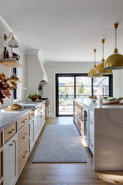 Eugene Pendants illuminate a white and tan kitchen island donning brass pulls and finished with a white quartz waterfall edge countertop.