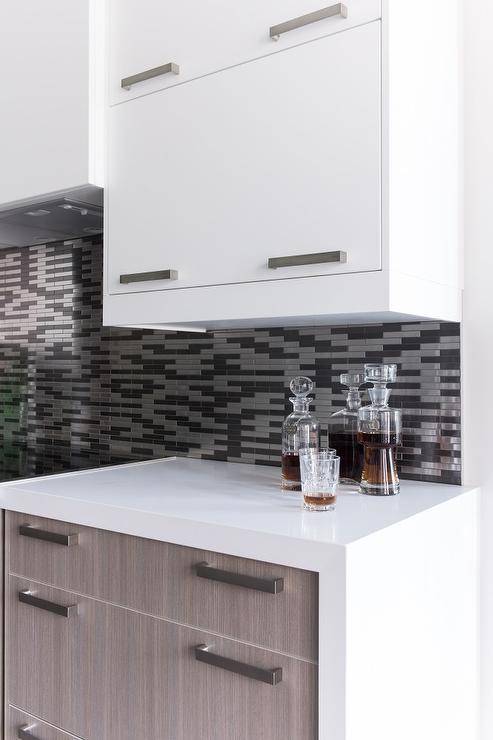 Fantastic two-tone kitchen boasts white flat front upper cabinets and brown oak veneer bottom cabinets adorned with nickel pulls paired with white quartz countertops and a silver and gray mosaic tile backsplash.