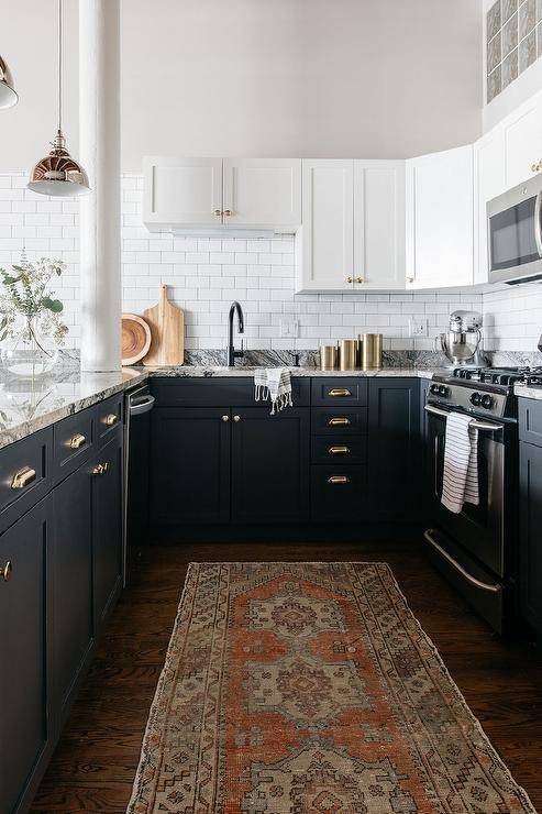 Black and white kitchen with two-toned cabinets and polished brass cup pulls boasting gray granite countertops and white subway tiles.