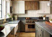 Kitchen features a reclaimed wood hood over a Wolf range with shiplap trim, two tone kitchen cabinets topped with gray marble and an apron sink with brass gooseneck faucet under wooden ceiling beams.