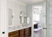 Chic master bathroom features a Restoration Hardware Victorian Hotel Pendant illuminating a seamless glass shower clad in marble. A linear marble tiled floor leads to a stained double washstand topped with white marble fitted with his and hers sinks placed under polished nickel pivot mirrors lining a mosaic marble tiled wall.