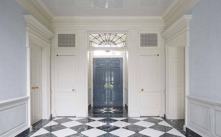 Black and white marble harlequin floor tiles lead to a vestibule boasting a a leaded glass transom window and a glossy blue French door.