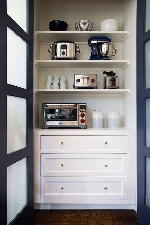 Kitchen pantry with blue bi-fold pantry doors and frosted glass panels. Small nickel knobs accent white shaker cabinet drawers under white stacked shelves displaying pantry essentials.