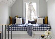 Attic window seat nook boasts a blue buffalo check cushion with various accent pillows and a gold faux bios accent table in a cottage home.