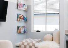 White and blue girl's room features a built in window seat with gray checkered throw under acrylic book ledges.