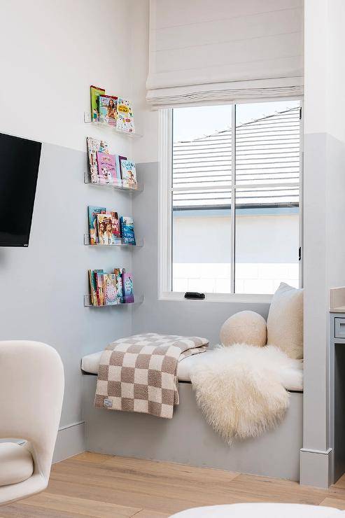 White and blue girl's room features a built in window seat with gray checkered throw under acrylic book ledges.